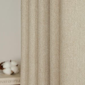 Puede incluir: Paneles de cortina beige con estampado de espiga. La tela tiene una apariencia texturizada con pliegues verticales. Las cortinas están hechas de un material de tono neutro, adecuado para varios estilos de diseño de interiores. El diseño es un patrón clásico y atemporal.