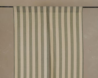 Puede incluir: Dos cortinas de rayas verticales en verde apagado y crema. Las rayas se alternan. Las cortinas cuelgan de una barra oscura contra una pared de tono neutro. La tela parece ser un material ligero y tejido.