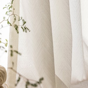 May include: White sheer curtains with a subtle chevron pattern. The curtains are made of a lightweight fabric and have a soft, drapey texture.