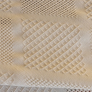 Puede incluir: Primer plano de una tela blanca tejida con un patr&oacute;n texturizado. La tela est&aacute; doblada por la mitad, revelando un patr&oacute;n diferente en la parte inferior.