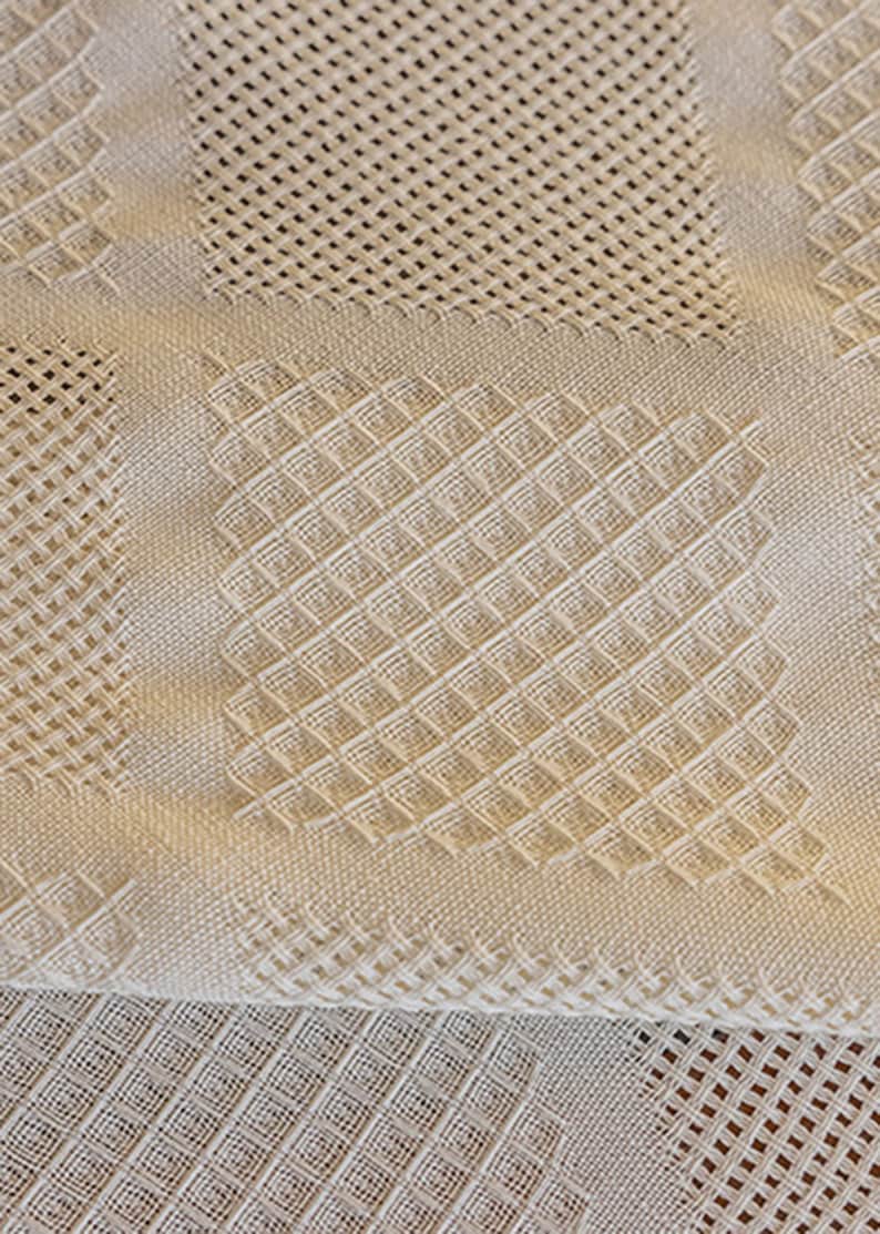 Puede incluir: Primer plano de una tela blanca tejida con un patr&oacute;n texturizado. La tela est&aacute; doblada por la mitad, revelando un patr&oacute;n diferente en la parte inferior.