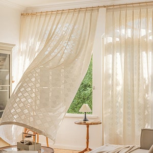 Puede incluir: Cortinas blancas y transparentes con un patr&oacute;n geom&eacute;trico cuelgan en una sala de estar con una mesa de madera y una l&aacute;mpara. Las cortinas se agitan con el viento.