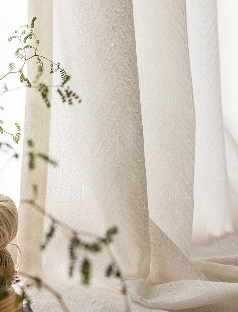 May include: White sheer curtains with a subtle chevron pattern. The curtains are made of a lightweight fabric and have a soft, drapey texture.