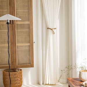 May include: White sheer curtains with a rope tieback, hanging in a room with a wicker cabinet and a floor lamp with a white paper shade.