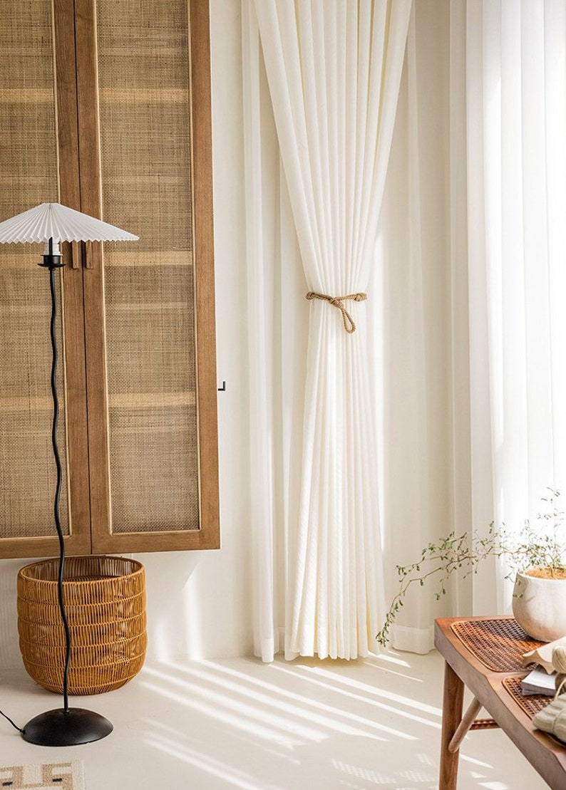 May include: White sheer curtains with a rope tieback, hanging in a room with a wicker cabinet and a floor lamp with a white paper shade.
