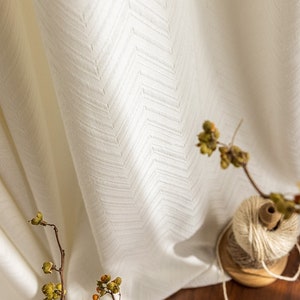 May include: White sheer curtains with a subtle herringbone pattern. The curtains are hanging in a window and are illuminated by natural light.