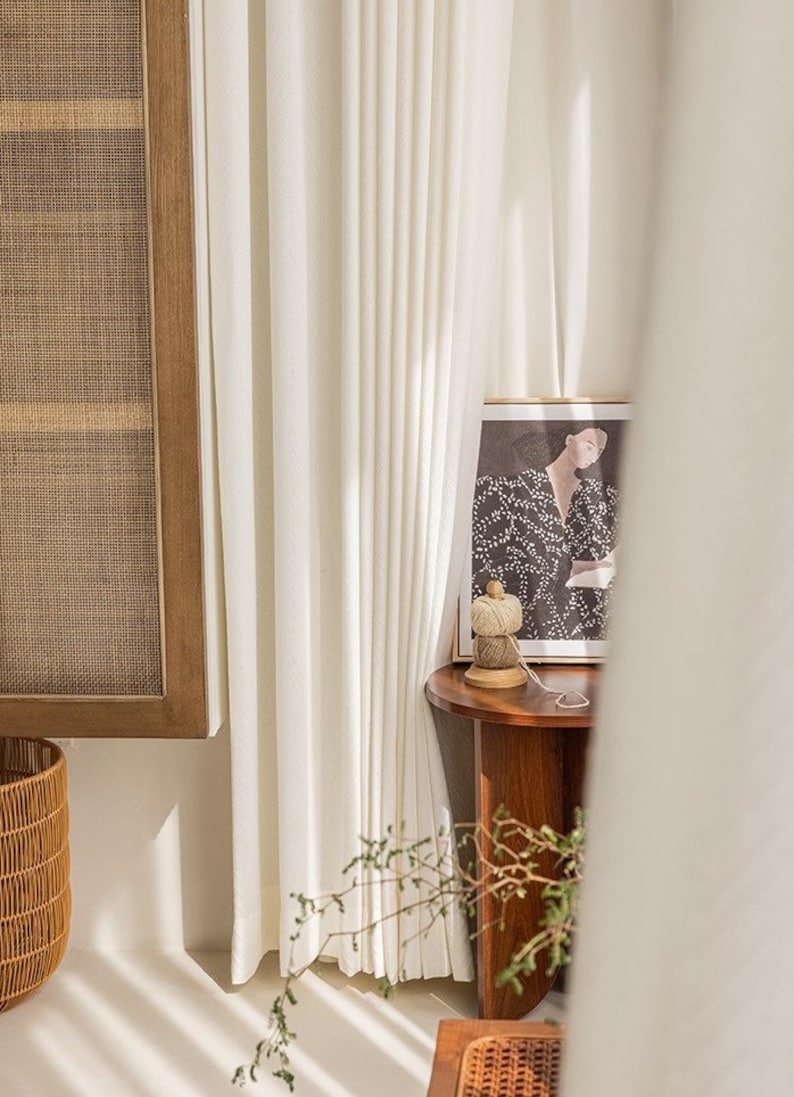 May include: White curtains with a wooden side table and a framed print of a woman in a black and white dress. The table has a spool of twine on it.