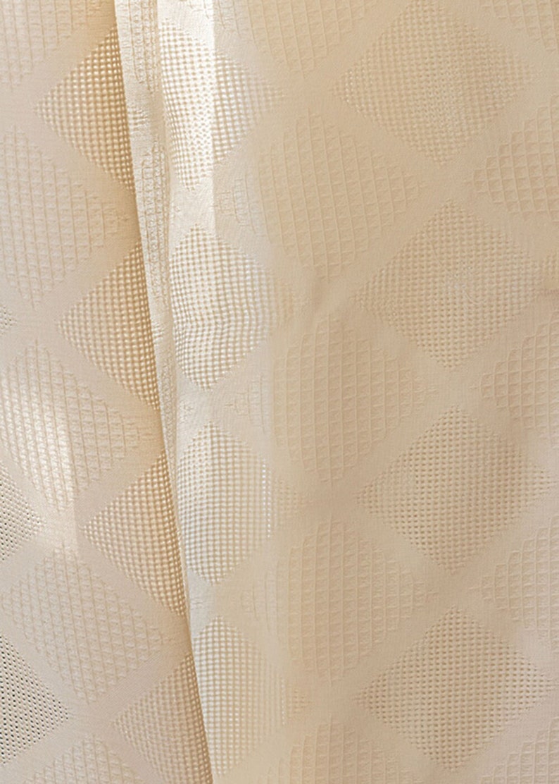 Puede incluir: Primer plano de una tela de color crema con un patr&oacute;n de forma de diamante. La tela tiene una textura sutil y una apariencia ligeramente transparente.