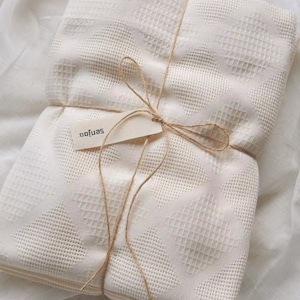 Puede incluir: Una pila de mantas blancas de tejido de gofre de algod&oacute;n atadas con cuerda y una etiqueta que dice "softjas".