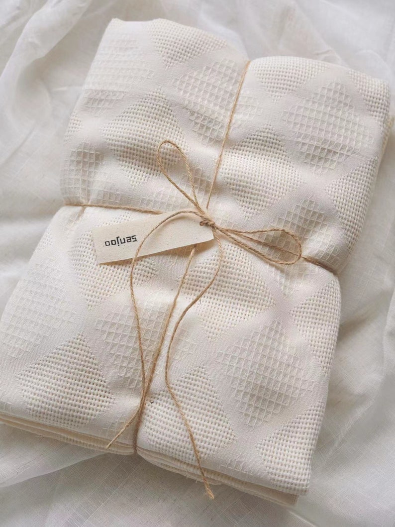 Puede incluir: Una pila de mantas blancas de tejido de gofre de algod&oacute;n atadas con cuerda y una etiqueta que dice "softjas".