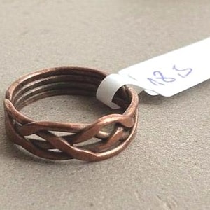 Könnte beinhalten: Ein kupferfarbener Ring mit geflochtenem Design. Der Ring hat ein gewebtes Muster auf der Vorderseite und mehrere Bänder auf der Rückseite. Ein weißes Etikett mit der Zahl "18,5" ist angebracht.