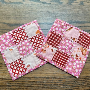 May include: Two pink and red patchwork fabric coasters with a floral pattern.