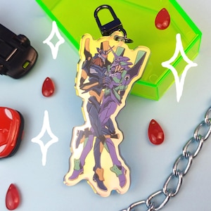 Pode incluir: Um chaveiro com uma ilustração colorida de dois personagens de anime, um com um terno preto e verde e o outro com um terno roxo e verde. O chaveiro é feito de metal e tem uma corrente prateada.