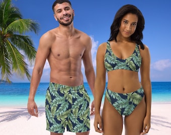 May include: A couple wearing matching tropical print swimwear. The man is wearing blue swim trunks with a green and white leaf pattern. The woman is wearing a green and white leaf pattern bikini top and matching bikini bottoms.
