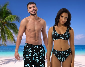 May include: A black two-piece bikini set and matching swim trunks with a light blue floral pattern. The swimwear is displayed on a beach with a blue sky and palm trees in the background.