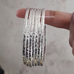 Pu&ograve; includere: Un set di sei braccialetti d'argento con una texture martellata. I braccialetti sono impilati uno sopra l'altro e sono tutti della stessa dimensione.