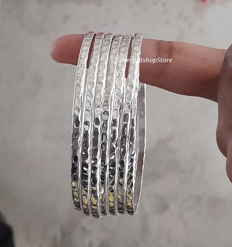 Pu&ograve; includere: Un set di sei braccialetti d'argento con una texture martellata. I braccialetti sono impilati uno sopra l'altro e sono tutti della stessa dimensione.