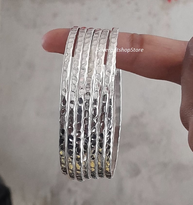 Pu&ograve; includere: Un set di sei braccialetti d'argento con una texture martellata. I braccialetti sono impilati uno sopra l'altro e sono tutti della stessa dimensione.