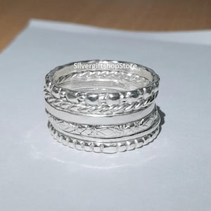 May include: A set of five silver stacking rings with different textures and patterns. The rings are all made of sterling silver and are designed to be worn together.