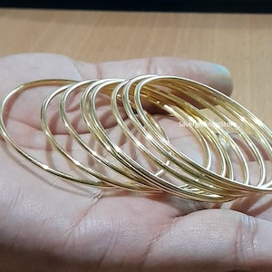 Puede incluir: Un conjunto de diez pulseras de brazalete de color dorado apiladas unas sobre otras.