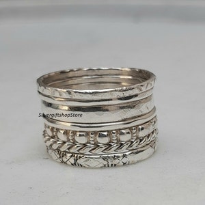 May include: A set of five silver stacking rings with different textures, including a beaded band, a rope-like band, and a band with a hammered finish. The rings are stacked on top of each other, creating a unique and stylish look.