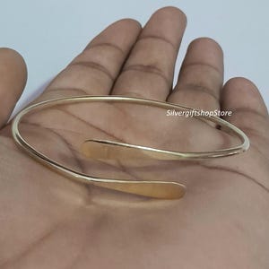 May include: A simple gold bangle bracelet with a curved design. The bracelet is open and has a smooth finish.