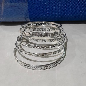 May include: Six silver bangles with different embossed designs. The bangles are stacked on top of each other.