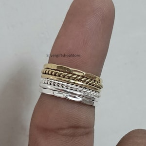 May include: A set of four stacking rings, two silver and two gold, worn on a finger. The rings are all different styles, including a hammered band, a rope design, and a plain band.