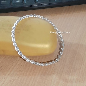 May include: A silver twisted bangle bracelet. The bracelet is made of a thick, twisted wire and is a simple, elegant design.