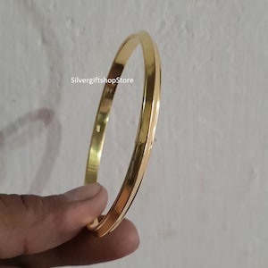May include: A gold bangle bracelet with a smooth, polished finish. The bracelet is about 1/2 inch wide and has a simple, classic design.