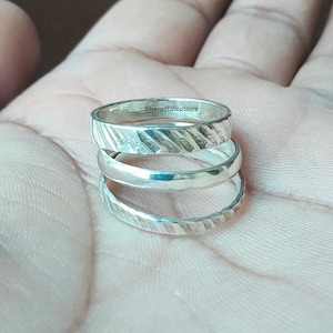 May include: Three silver rings stacked on top of each other. The top ring has a textured design and the inscription "SilvergiftshopStore".