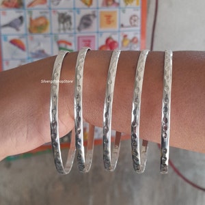 May include: Five silver bangles with a hammered texture and a row of small circles along the edge.