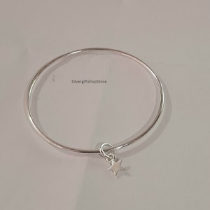 Op de afbeelding: Een zilveren armband met een klein sterretje dat eraan hangt. SilvergiftshopStore is gedrukt op de witte achtergrond.