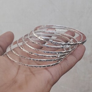 Pu&ograve; includere: Un set di sette braccialetti d'argento con una texture martellata. I braccialetti sono impilati uno sopra l'altro e sono tutti della stessa dimensione.