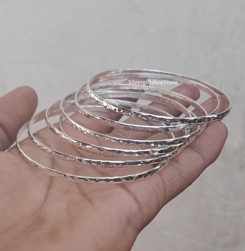 Pu&ograve; includere: Un set di sette braccialetti d'argento con una texture martellata. I braccialetti sono impilati uno sopra l'altro e sono tutti della stessa dimensione.