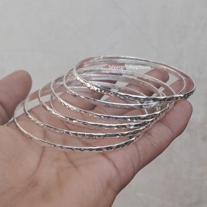 Pu&ograve; includere: Un set di sette braccialetti d'argento con una texture martellata. I braccialetti sono impilati uno sopra l'altro e sono tutti della stessa dimensione.