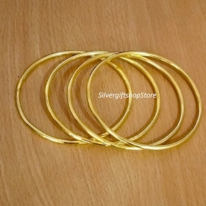 May include: Four gold-coloured metal bangles stacked together. The bangles are smooth and shiny.