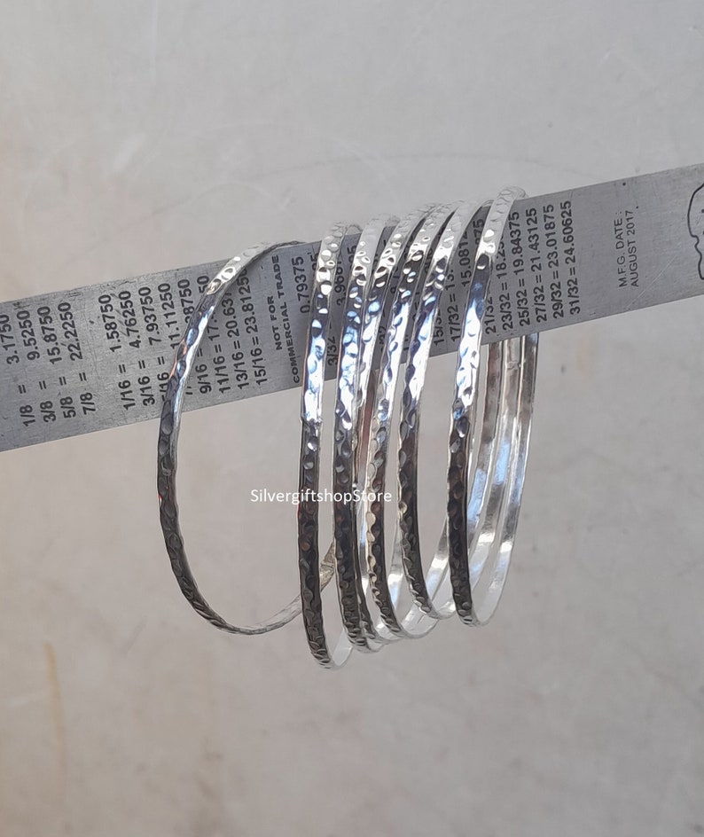 Pu&ograve; includere: Un set di otto braccialetti in argento martellato. I braccialetti sono impilati uno sopra l'altro e hanno tutti la stessa larghezza. I braccialetti sono in argento e hanno una finitura martellata. I braccialetti sono di dimensioni diverse, con il braccialetto pi&ugrave; piccolo che ha un diametro di 3,175 mm e il braccialetto pi&ugrave; grande che ha un diametro di 24,60625 mm.