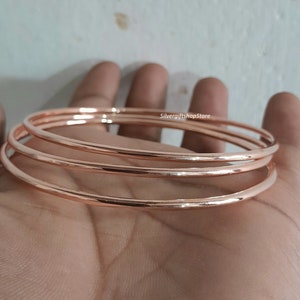 Könnte beinhalten: Ein Satz aus vier roségoldenen Armreifen, die übereinander gestapelt sind. Die Armreifen sind glatt und glänzend.