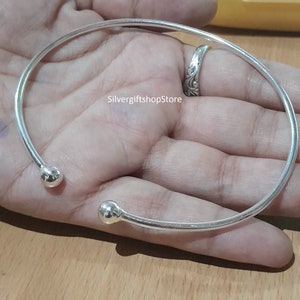 May include: A silver bangle bracelet with two round ends. The bracelet is open and has a simple design.