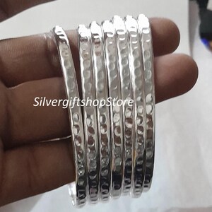 Pu&ograve; includere: Un set di sei braccialetti d'argento con una texture martellata. I braccialetti sono impilati uno sopra l'altro e hanno una finitura lucida.