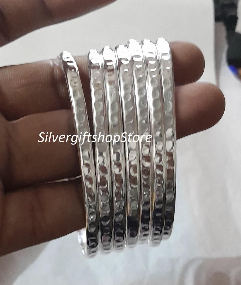 Pu&ograve; includere: Un set di sei braccialetti d'argento con una texture martellata. I braccialetti sono impilati uno sopra l'altro e hanno una finitura lucida.