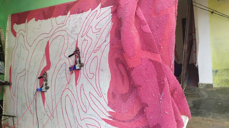 May include: A large pink fabric with a white design is being worked on with two sewing machines. The fabric is hanging on a wall and the machines are attached to the fabric with cords.