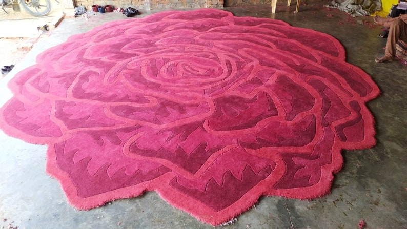 May include: A large, round, pink and red rose-shaped rug. The rug is made of a soft, plush material and has a detailed design.