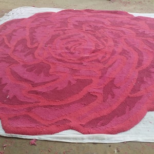May include: A large, pink rose rug made of fabric. The rug is laid out on a white cloth.