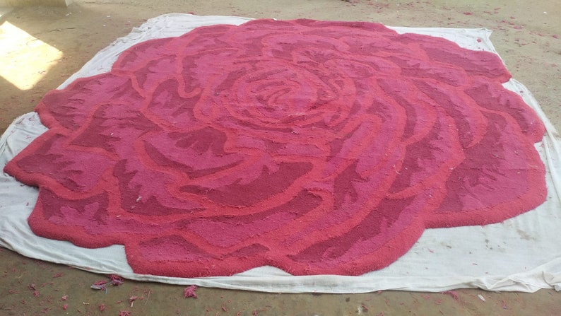 May include: A large, pink rose rug made of fabric. The rug is laid out on a white cloth.