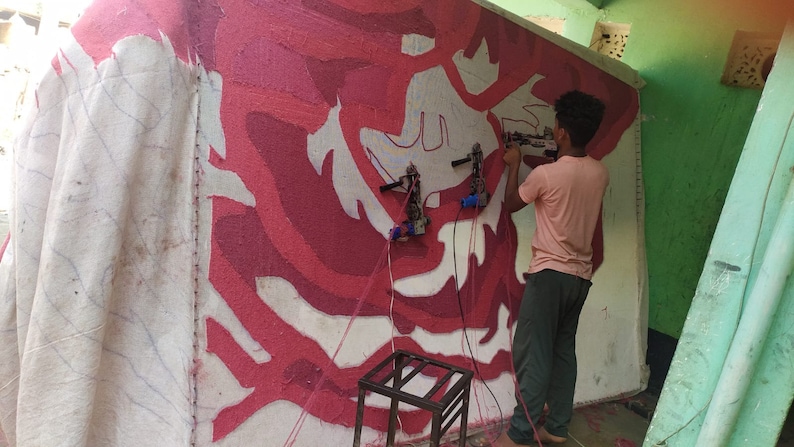 May include: A person uses a tool to create a large-scale abstract art piece on a wall. The art features a white background with red and pink abstract shapes.