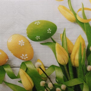 2 of 4 stuks papieren servetten voor decoupage, gele en groene paaseieren, satijnen lint en gele tulpen op lichtgrijze plankenachtergrond