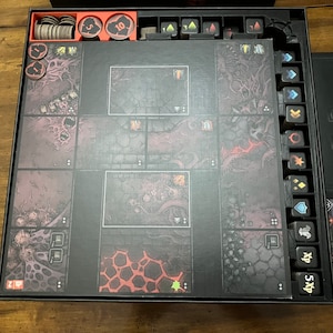 K&ouml;nnte beinhalten: Ein Brettspiel-Set mit einem dunklen, dungeonartigen Thema. Das Spielbrett ist in quadratische Kacheln mit detaillierten Illustrationen unterteilt. Enth&auml;lt verschiedene Spielsteine, W&uuml;rfel und Kartenhalter. Die Farbpalette ist haupts&auml;chlich dunkelgrau, schwarz und rot.