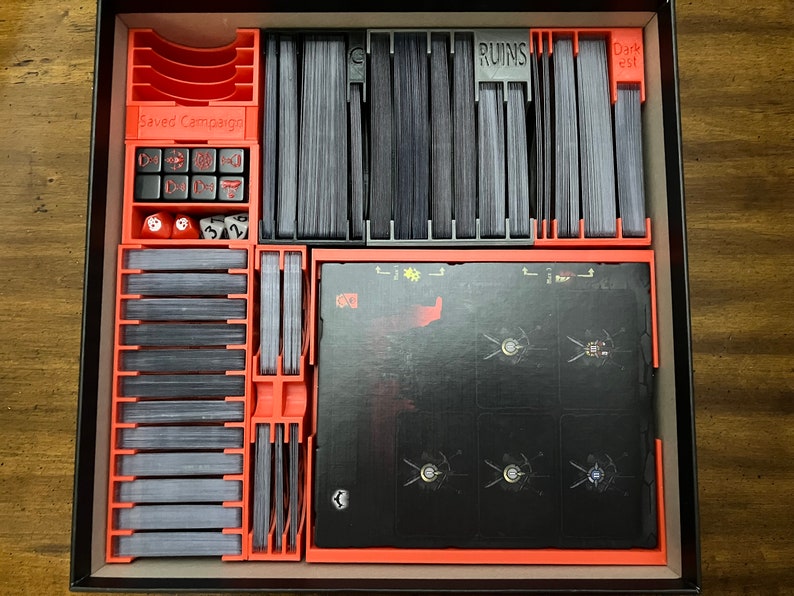 K&ouml;nnte beinhalten: Ein orange-grauer Spiel-Organizer f&uuml;r ein Brettspiel. Der Organizer hat F&auml;cher f&uuml;r Karten, W&uuml;rfel und andere Spielkomponenten. Die Texte "Saved Campaign", "Ruins" und "Darkest" sind sichtbar.